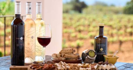 A photo of a table set with a platter of cold cuts and bottles of wine, with a vineyard in the background.