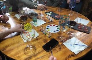 Imagen de una mesa con copas de vino y pinturas para decorar las copas de vino.