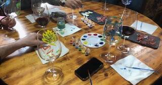 A photo of a table with wine glasses and paints for decorating the wine glasses.